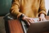 Working person with orange sweater works on laptop