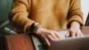 Working person with orange sweater works on laptop