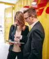 Two colleagues are standing in front of a yellow DHL container and discussing something on their tablets