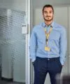 DHL employee with blue shirt stands in front of glass wall and looks into camera