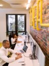 Three people work in the office with brick accent wall